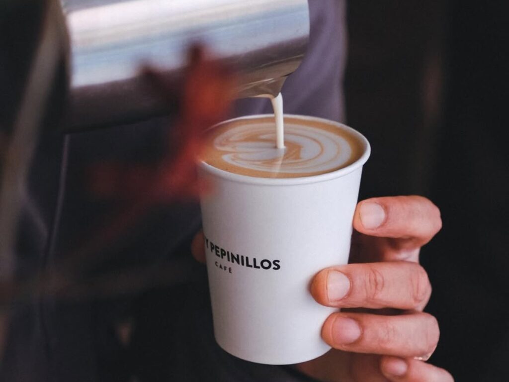 Barista pouring milk into a takeaway cup at Pan y Pepinillos Café, specialty coffee shop in Madrid